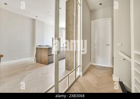 Intérieur spacieux et minimaliste décloisonné avec parquet à chevrons, piliers en miroir et murs blancs élégants. Banque D'Images