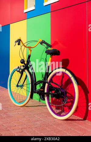 Un vélo coloré s'appuie contre un mur urbain peint de couleurs vives présentant un éventail dynamique de couleurs primaires et secondaires Banque D'Images