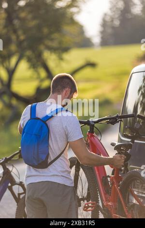 Le jeune homme décharge les vélos de montagne électriques, pour lui et sa petite amie, les soulevant de la galerie d'attelage du véhicule. Banque D'Images