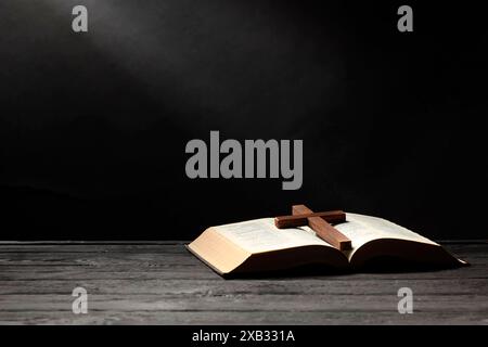 Bible et croix sur la table en bois gris sur fond sombre, espace pour le texte. Religion du christianisme Banque D'Images