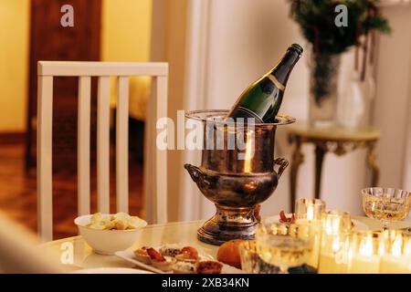 Gros plan d'un seau à glace et d'une bouteille de champagne sur une table de fête couverte. Bougies allumées, verres de vin mousseux et en-cas sur le dîner Banque D'Images