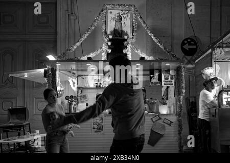 L'homme danse ivre devant sa femme et son enfant dans un stand de boissons décoré pendant les festivités de l'alfama, avec une image de San Antonio ornée au-dessus Banque D'Images