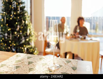 Un gros plan d'un élégant verre sur une longue tige avec du champagne sur la table dans la salle à manger à la maison. Vin mousseux dans un gobelet. Une Christma décorée Banque D'Images