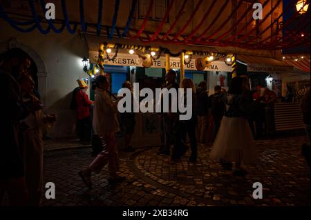 Les gens se rassemblent autour d'un stand de nourriture festif à Alfama pendant les festivités populaires des Saints, avec des décorations étincelantes et des lumières ajoutant à la scène Banque D'Images