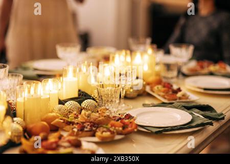 Une table de fête couverte avec décor du nouvel an. Bougies allumées, collations, boules de Noël, assiettes et verres sur la nappe. Une fête de Noël. Un fest Banque D'Images