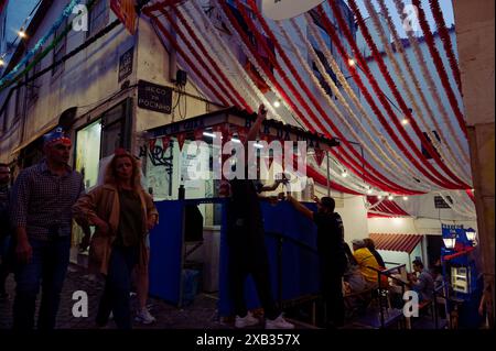 Les fêtards passent devant un stand de nourriture et de boissons animé sous des décorations colorées pendant les festivités populaires des Saints dans le quartier d'Alfama Banque D'Images