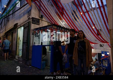 Les fêtards passent devant un stand de nourriture et de boissons animé sous des décorations colorées pendant les festivités populaires des Saints dans le quartier d'Alfama Banque D'Images