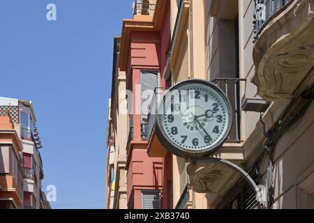 Gros plan d'une vieille horloge analogique qui montre 14h et est suspendue à l'un des bâtiments sur une rue Banque D'Images