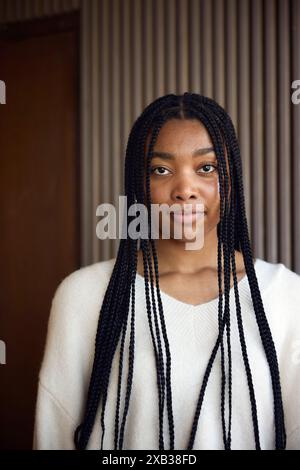 Femme souriante avec des cheveux tressés contre le mur Banque D'Images