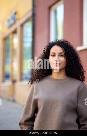 Femme aux cheveux bouclés souriante debout contre le bâtiment Banque D'Images