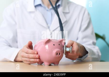 Docteur avec tirelire et stéthoscope à la table en bois, gros plan Banque D'Images