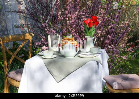 Beau bouquet de tulipes et gaufres fraîchement cuites sur table servi pour boire du thé dans le jardin Banque D'Images