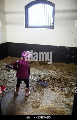 Vue arrière du garçon nettoyant l'herbe sèche de l'étable Banque D'Images