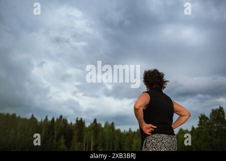 Vue en angle bas de la femme debout avec les bras akimbo et regardant le ciel Banque D'Images
