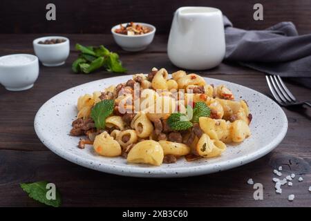 Pâtes cuites avec du bœuf haché et des légumes, macaronis de style marine sur une assiette. Fond en bois foncé Banque D'Images