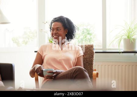 Femme mature avec tasse à café assise sur la chaise à la maison Banque D'Images