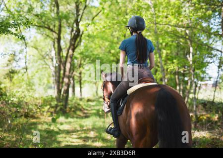 Vue arrière d'une femme jockey chevauchant un cheval vers des arbres verts Banque D'Images