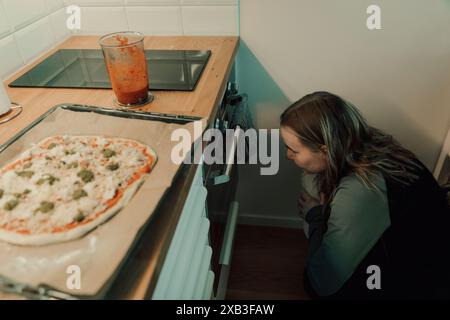 Vue en angle élevé de la jeune femme accroupie tout en regardant le four sous le comptoir de cuisine à la maison Banque D'Images