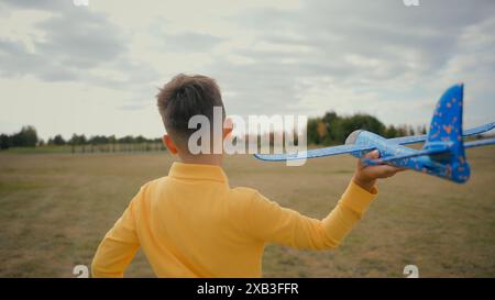 Vue arrière adorable enfant caucasien petit garçon fils écolier jog adolescent jouer avec un avion jouet à l'extérieur beau champ de parc naturel. Enfant jouant au lancer de course Banque D'Images