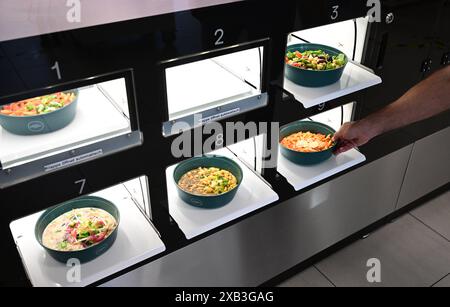 10 juin 2024, Bade-Württemberg, Tübingen : les aliments fraîchement préparés sont collectés dans un distributeur automatique dans une cantine de l'hôpital universitaire de Tübingen. Selon l’hôpital universitaire, c’est le premier endroit au monde à utiliser le robot de cuisson de la start-up de Hambourg goodBytz. Cinq plats asiatiques, allemands et italiens sont proposés tous les jours, ainsi que des plats de Street food. Photo : Bernd Weißbrod/dpa Banque D'Images