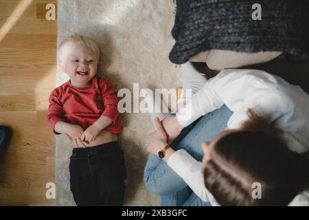 Directement au-dessus de la vue de la mère assise par le fils heureux couché sur la moquette à la maison Banque D'Images