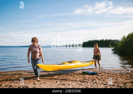 Mère et fille transportant des kayaks à la rive le jour ensoleillé pendant les vacances Banque D'Images