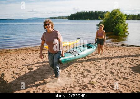 Femmes portant des kayaks à la rive de la rivière le jour ensoleillé pendant les vacances Banque D'Images