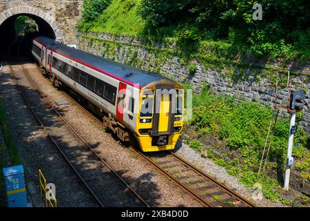 Conwy Wales UK 06-01-2024. Train de voyageurs émergeant d'un tunnel entouré de verdure et de murs de pierre par une journée ensoleillée. Banque D'Images