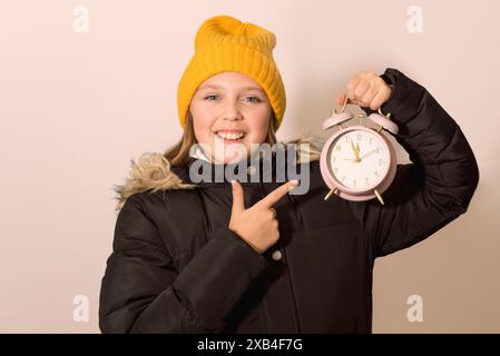 Concept d'hiver du nouvel an. Adolescente avec un grand vieux réveil de bureau. Cinq minutes à douze. Fond de fuzz pêche Banque D'Images