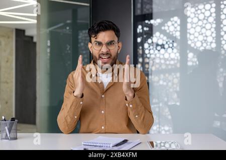 Jeune homme professionnel montrant la frustration et la colère dans un bureau moderne. Expression émotionnelle du stress et des difficultés au travail. Banque D'Images