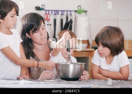 Mère apprend à ses enfants à faire un gâteau. Les enfants apprennent à mélanger les ingrédients. Enfants dans la cuisine Banque D'Images