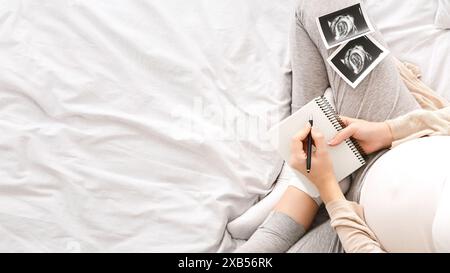 Femme enceinte se relaxant dans le lit, prenant des notes avec des photos échographiques Banque D'Images