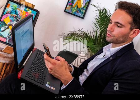 Masculin Urban Professional jeune adulte et professionnel gay travaillant avec son ordinateur portable et son smartphone dans un café pour aider ses clients avec leur marketing en ligne et seo. Berlin, Allemagne. MRYES Berlin les verts, le café et les plantes berlin Allemagne Copyright : xGuidoxKoppesxPhotox Banque D'Images