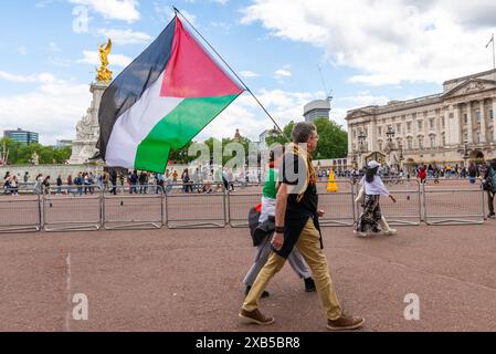 Des manifestants pro-Palestine passent devant le Mémorial Victoria et le Palais de Buckingham à Londres, au Royaume-Uni, avec un grand drapeau palestinien Banque D'Images