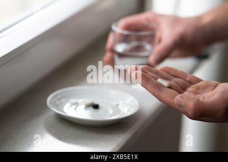 gros plan des mains masculines tenant la pilule de capsule et le verre d'eau. Médecine pharmacie santé. gros plan d'un homme prenant des pilules Banque D'Images