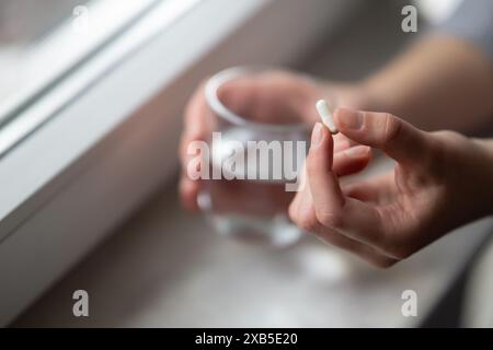 les mains de la femme tenant la pilule de capsule et le verre d'eau se rapprochent Banque D'Images