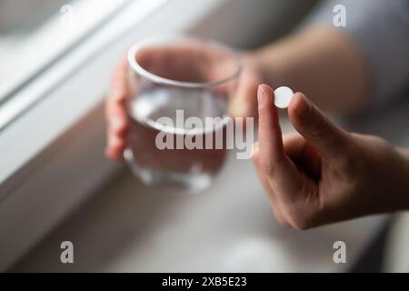 les mains de la femme tenant la pilule et le verre d'eau se rapprochent Banque D'Images