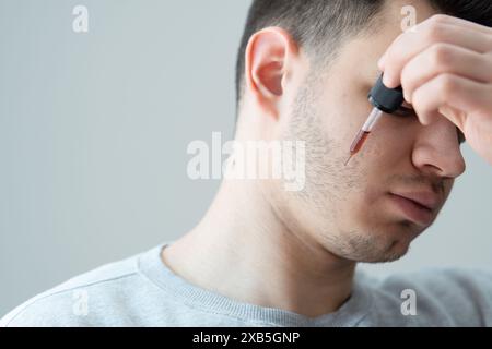 jeune homme appliquant l'huile de croissance de barbe avec pipette gros plan. homme tenant la pipette avec de l'huile pour la barbe, appliquant le sérum cosmétique avec la pipette sur le visage Banque D'Images