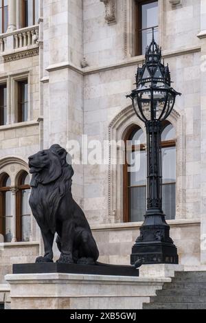 Statue en bronze d'un lion devant le magnifique bâtiment ancien du Parlement hongrois dans un style néo-gothique à Budapest Banque D'Images