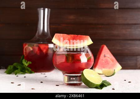 Verre et bouteille de limonade de pastèque fraîche avec citron vert sur table blanche Banque D'Images