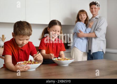 Petits enfants avec leurs parents prenant le petit déjeuner avant l'école dans la cuisine Banque D'Images