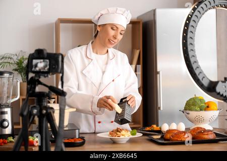 Blogueuse culinaire râpant du fromage sur des pâtes tout en enregistrant une vidéo dans la cuisine Banque D'Images