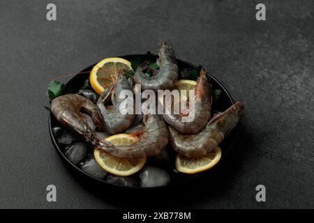 Grosses crevettes royales sur tranches de citron et glace. Plaque noire. Fond noir Banque D'Images