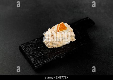 Rouleau de meringue. Protéines fouettées et sucre, garniture - fromage à la crème à base de fromage à pâte molle et de crème sur une planche à découper noire Banque D'Images