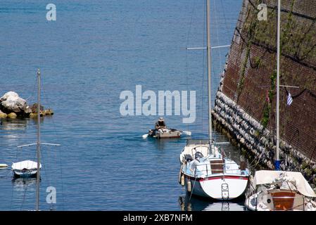 Peu de petits bateaux dans une eau bleue sereine avec des rochers et une jetée Banque D'Images