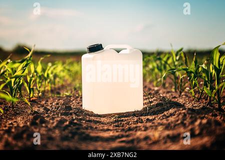 Canister blanc vierge d'herbicide dans le champ de semis de maïs au coucher du soleil de printemps, foyer sélectif Banque D'Images