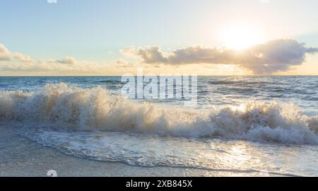 Une vue panoramique sur l'océan avec des vagues qui s'écrasent sur la plage au coucher du soleil Banque D'Images