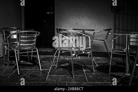 Café extérieur vide avec chaises et tables en métal en B&W, créant une atmosphère sobre et minimaliste. pas de corps. Banque D'Images