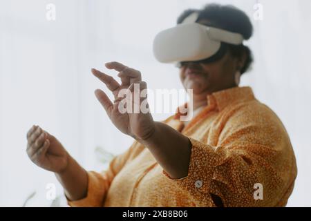 Photo moyenne en gros plan d'une femme afro-américaine senior imaginant qu'elle touche des choses dans l'air à l'aide d'un casque VR Banque D'Images