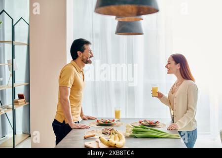 Une femme rousse et un homme barbu préparent un repas ensemble au comptoir de la cuisine de leur appartement moderne. Banque D'Images